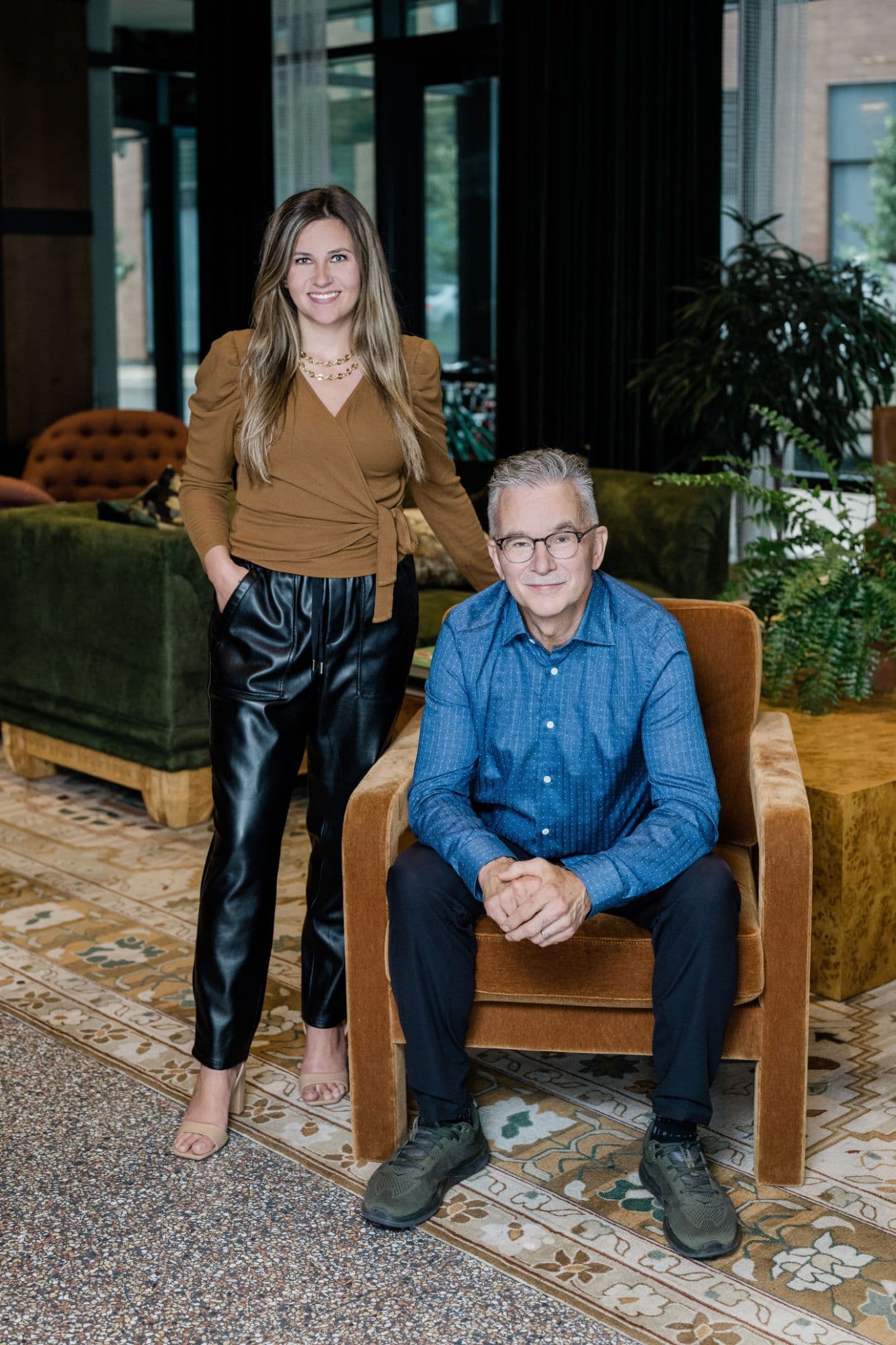 Theresa Casey standing beside her father and business partner, Eddie Cloutier, who is seated in a velvet armchair